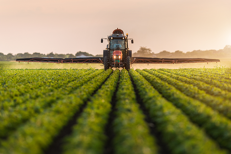 Image: A tractor spraying a field of crops with pesticides