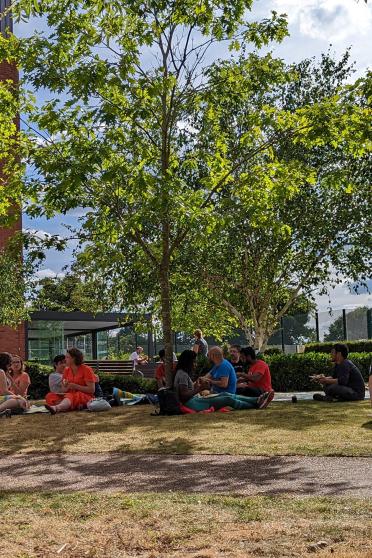 EI Staff and students sitting on the grass outside the Earlham Institute building
