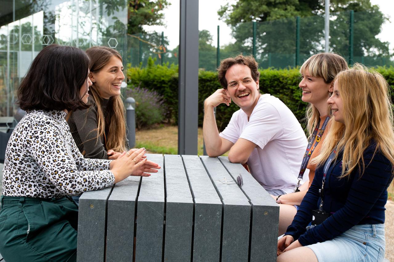 Students from the Earlham Institute Student Body sitting outside round a picnic bench in the summer.