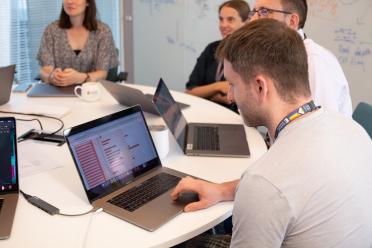 Photo shows weekly group meeting, with members of the group gathered around a circular table in discussion.