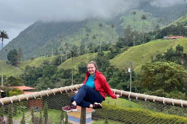 Kate Denning James, sitting cross legged on a netted outcrop, overlooking a lush green valley in Colombia