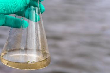 Conical flask containing river water samples, showing murky water with detritus in
