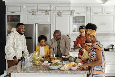 A family gathers round a kitchen table with food spread out