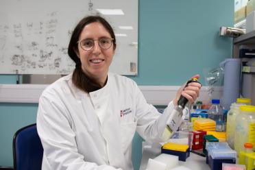 Dr Sarah Guiziou photographed siting down facing the camera, in a white lab coat holding a multi channel pipette.