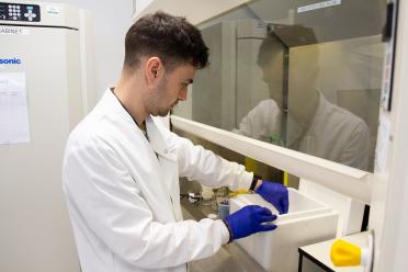 Jonathan wearing a white lab coat and blue safety gloves, handling dry ice under a fume hood in the lab.