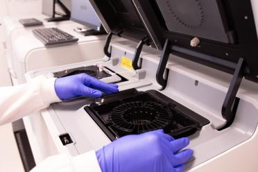 A scientist wearing blue safety gloves operates the Vizgen MERSCOPE machine