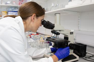 Dr Sally Warring, Protistologist in the Neil Hall Group at a microscope in the labs at EI