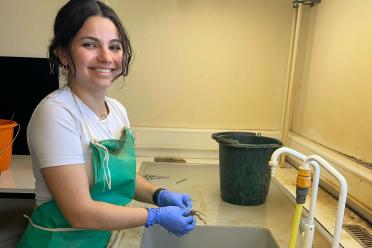 Marine wearing a green apron and blue safety gloves at a lab sink