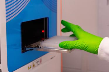 Scientist wearing green safety gloves loads a plate into the Echo acoustic liquid handler