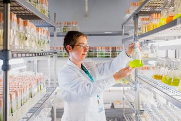 Scientist wearing white lab coat in a storage facility with shelves full of water and algae samples in clear jars