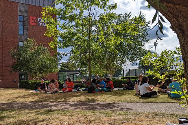 EI Staff and students sitting on the grass outside the Earlham Institute building