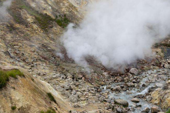 Steam over hot geothermal springs in a mountain gorge.